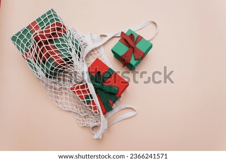 Gifts with ribbons are in a white eco-friendly string bag on a beige background. Top view. Copy space.