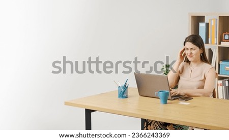 Woman sitting at the desk and working with her laptop, she is exhausted and she is having a headache