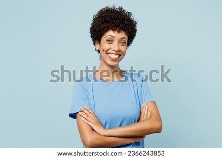 Young smiling happy woman of African American ethnicity wear t-shirt casual clothes holding hands crossed folded isolated on plain pastel light blue cyan background studio portrait. Lifestyle concept