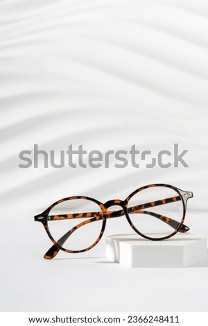 Trendy eyewear photography. Eye glasses creative concept. Classic tortoiseshell frame glasses on a podium on a white background. Minimal still life. Vertical. Copy space. Optic store discount, sale.