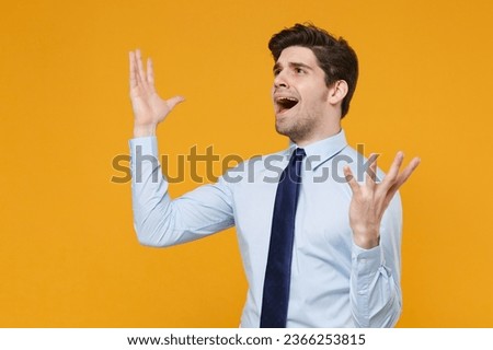 Shocked young business man in classic blue shirt tie posing isolated on yellow background. Achievement career wealth business concept. Mock up copy space. Spreading hands, screaming, looking aside