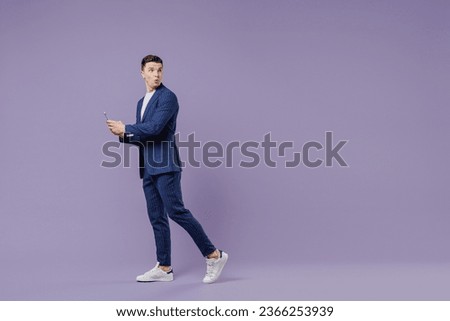 Full size young successful employee business man lawyer 20s wear formal blue suit white t-shirt move stroll hold use mobile cell phone look back isolated on pastel purple background studio portrait