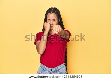 Young Indonesian woman on yellow studio backdrop throwing a punch, anger, fighting due to an argument, boxing.