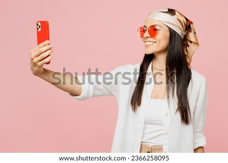 Young latin woman wear white shirt casual clothes sunglasses doing selfie shot on mobile cell phone post photo on social network isolated on plain pastel light pink background studio Lifestyle concept
