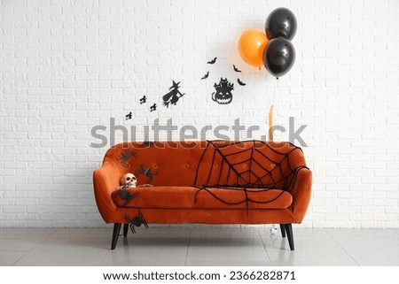 Stylish sofa, balloons and Halloween decor near light brick wall in room
