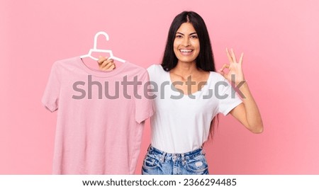 hispanic pretty woman feeling happy, showing approval with okay gesture and holding a choosen cloth