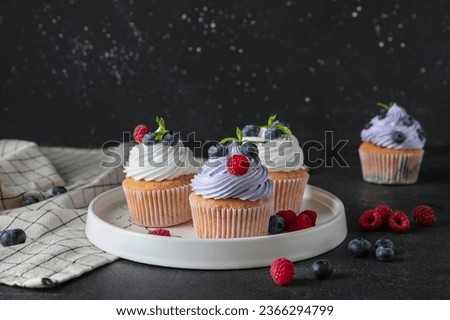 Plate of delicious cupcakes with blueberries, raspberries and mint on black background Royalty-Free Stock Photo #2366294799