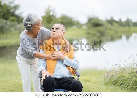 Happy Life Retirement, Asian Elderly wife take care husband sitting on wheelchair with warm cloth in the park relaxing with love, Senior couple take care of each other.
