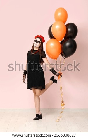 Young woman dressed for Halloween with balloons near light wall