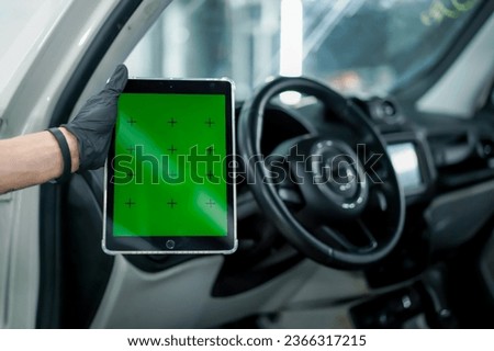 Close-up of a hand holding a tablet on which a green screen is open against the background of car interior