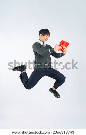 Asian male student jumping while reading a book in a white background studio.
