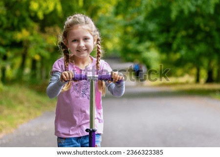 Portrait of a cute, blonde girl with her scooter in a park