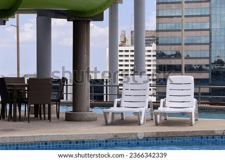 a photography of a pool with chairs and a table in it, terrace with chairs and tables near a pool with a view of a city.