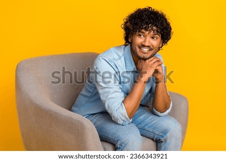 Photo of toothy beaming man dressed with curly hair denim shirt sit in armchair look empty space isolated on yellow color background Royalty-Free Stock Photo #2366343921