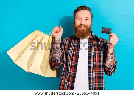 Portrait of good mood satisfied man with tattoo wear plaid shirt holding shopping bags debit card isolated on blue color background
