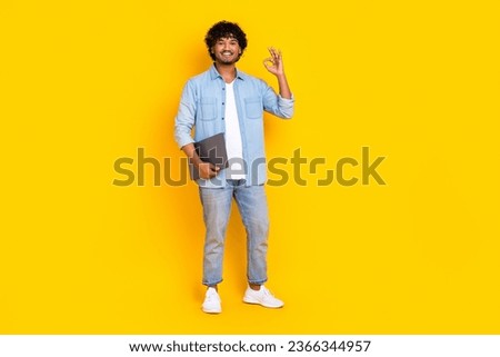 Full size photo of clever man dressed denim shirt stylish jeans hold laptop show thumb up good work isolated on yellow color background