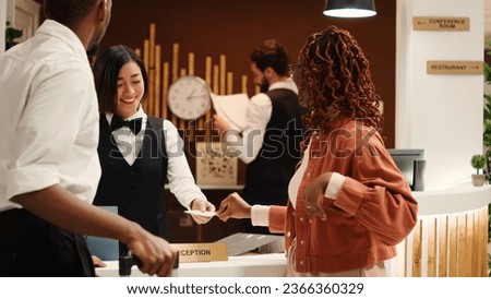 Tourists finishing vacation trip, handing out room card key to cheerful friendly receptionists during check out process. Happy guests preparing to leave hotel after nice stay Royalty-Free Stock Photo #2366360329