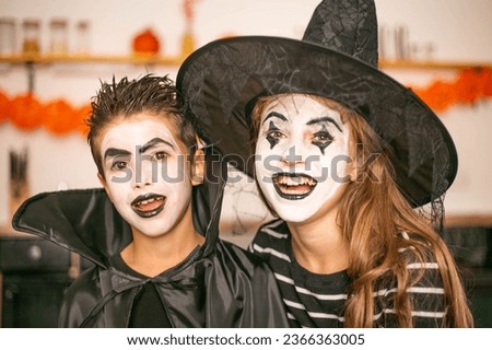 Photo close-up of faces. Two children having fun smiling, dressed in witch and vampire costumes ready for Halloween with makeup. Brother and sister look at the camera and laugh. Process of preparing 