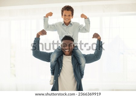 We Are Strong. African American Dad Holding His Little Son On Neck And Showing Their Biceps, Teaching Kid To Be A Leader At Home, Demonstrating Strength. Raising Little Champion Concept Royalty-Free Stock Photo #2366369919