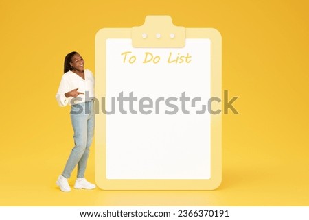 Glad young black woman in casual point finger at big plan with empty space, to do list, isolated on yellow studio background. Recommendation future planning, motivation and lifestyle, work, study