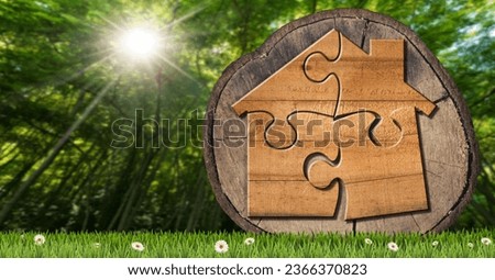 Wooden house made of jigsaw puzzle pieces on a cross section of a tree trunk, on a green meadow with daisy flowers and a green forest on background. Royalty-Free Stock Photo #2366370823