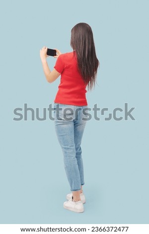 Young fit woman using smartphone and taking pictures, back view, full length
