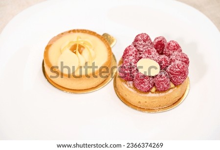 Beautiful still life with French baked tartlet with lemon meringue and partial view of raspberry cake, isolated on white studio background. Advertising photography.