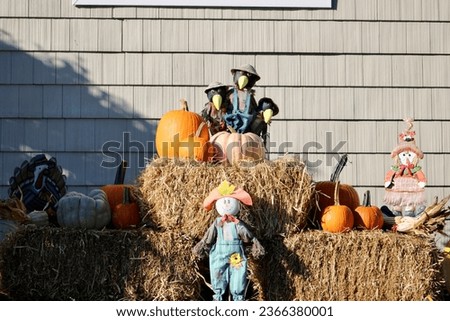 A festive fall display. There are three bales of hay, a flag that reads "Happy Fall Y'All", pumpkins, and decorations in the ground.