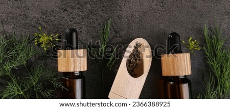 Bottles of dill essential oil and wooden scoop on wooden table against grey background, flat lay. Banner design