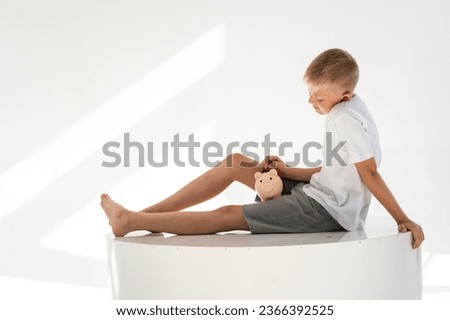 A boy with a piggy bank in his hands on a white background. Concept of finances and family budget. Bright and sunny picture.