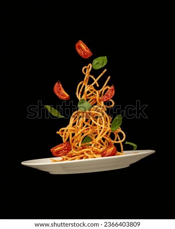 Pasta falling into a plate with tomatoes and basil on a black background. Levitation Royalty-Free Stock Photo #2366403809