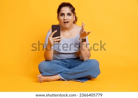 Young smiling happy woman in casual trendy clothing using mobile cell phone looks confused  isolated on orange background studio. People lifestyle concept