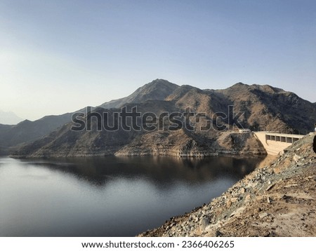 A beautiful daytime view of  Wadi Qanuna Dam in Al Bahah, Saudi Arabia. The water of the dam and the surrounding hills are presenting a beautiful scene in the sunlight.