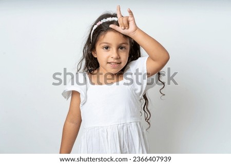 young beautiful kid girl making fun of people with fingers on forehead doing loser gesture mocking and insulting.
