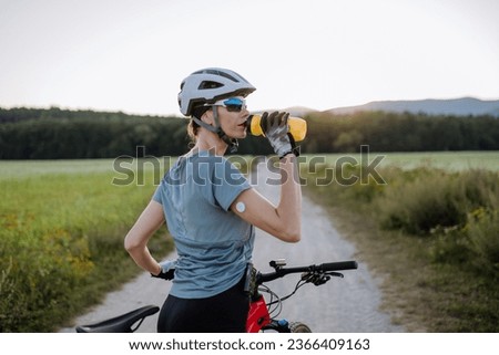Diabetic cyclist with a continuous glucose monitor on her arm drinking water during her bike tour. Royalty-Free Stock Photo #2366409163