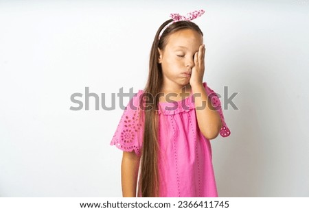 Tired overworked beautiful kid girl wearing pink dress  has sleepy expression, gloomy look, covers face with hand, has eyes shut, gasps from tiredness, fatigue after party