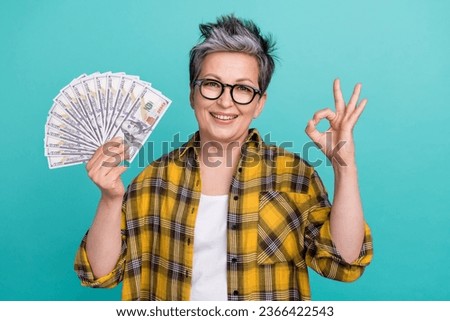 Photo portrait of charming grandmother hold money fan okey symbol wear trendy plaid yellow outfit isolated on cyan color background