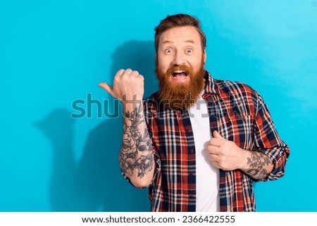 Portrait of astonished ecstatic man with tattoo wear plaid shirt indicating at amazing offer empty space isolated on blue color background