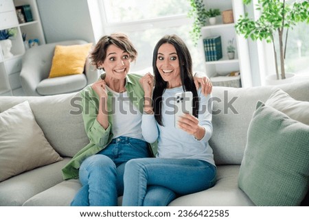 Photo of shocked lucky young ladies dressed shirts sitting couch shopping apple samsung iphone modern device indoors house room