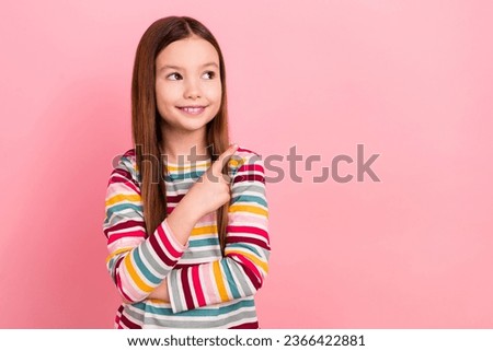 Photo of cheerful dreamy small daughter girl pointing finger empty space information mockup brand logo isolated on pink color background