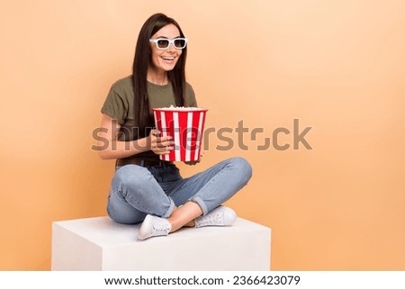 Full length photo of cheerful positive girl dressed khaki t-shirt eating pop corn watching movie empty space isolated beige color background