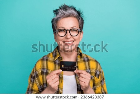 Photo of attractive retired woman hold credit card banker dressed stylish checkered yellow clothes isolated on aquamarine color background