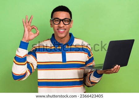 Photo portrait of handsome young guy showing okey symbol netbook dressed stylish striped outfit isolated on green color background