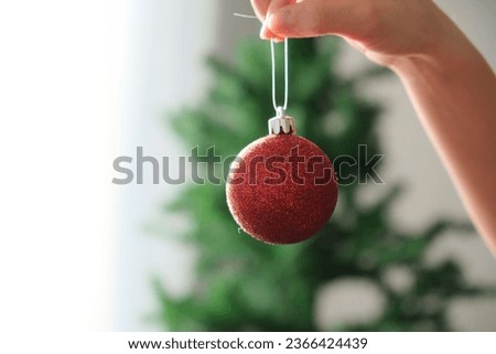 Close up woman holding red Christmas ornament on Christmas tree and white background.