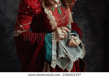 Closeup on medieval queen in red dress with handkerchief on dark gray background.