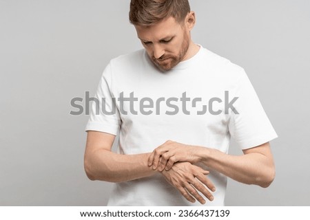 Man touching wrist of hand feeling pain on gray background. Tunnel syndrome, neuralgia, pinched nerve in arm after injury, consequences of computer work. Health problems, discomfort, symptom concept. Royalty-Free Stock Photo #2366437139