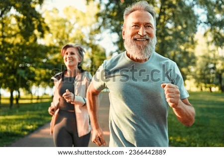 Cardio training. Close up of energetic fit sportsman spending morning in park and jogging together with wife. Active pensioners taking care of health and doing regular physical activities on nature. Royalty-Free Stock Photo #2366442889