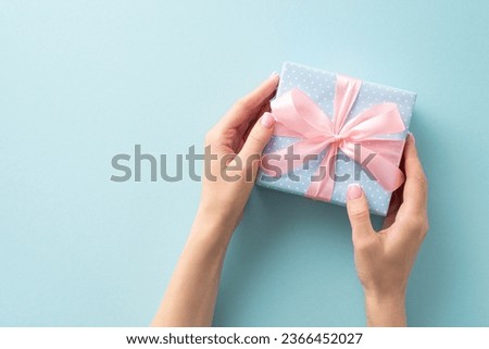 The art of gifting: From first person top view, girl presents a pastel blue gift box adorned with polka dots and a pink ribbon bow, against a pastel blue backdrop for your personal touch
