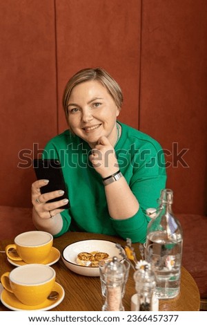 Plus size woman with smartphone in cafe. Female blogger, online work