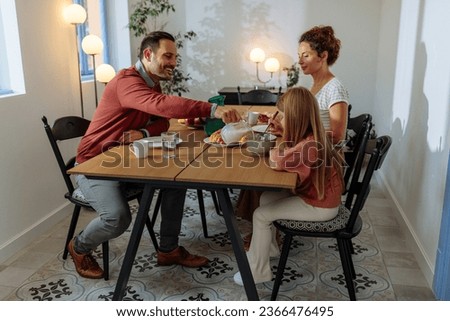 Family having a breakfast at their home while father is pouring milk into daughters cereal at the dining table